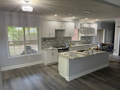 Modern kitchen with white cabinets, gray backsplash, and island, with gray flooring and a window.