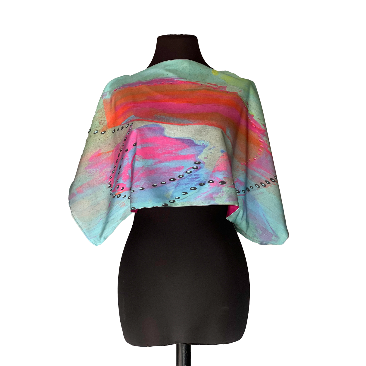Colorful cropped shawl on a black mannequin, with blue, pink, and orange paint and silver studs along the edges.