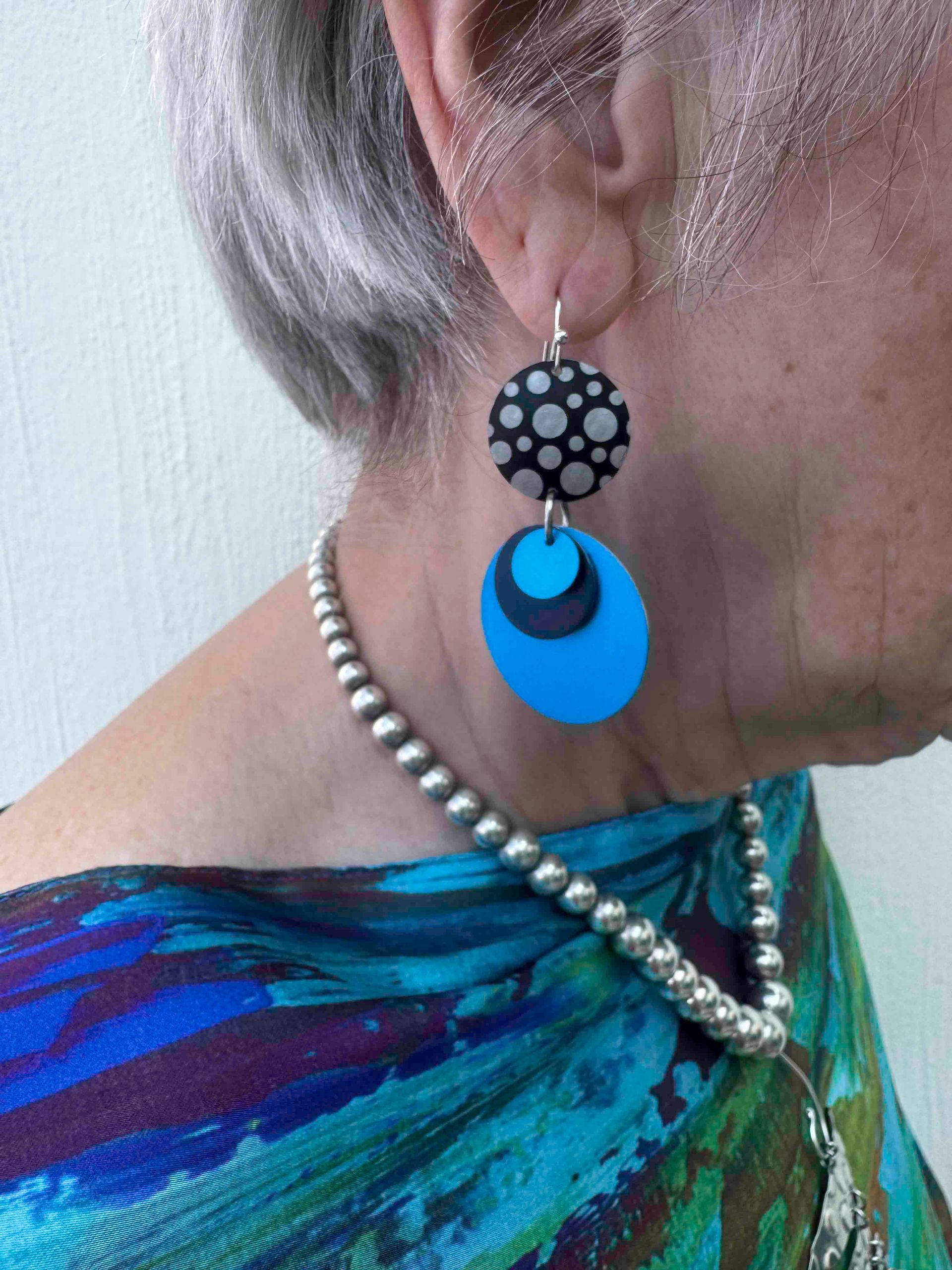 Woman wearing patterned earrings and beaded necklace, blue scarf.