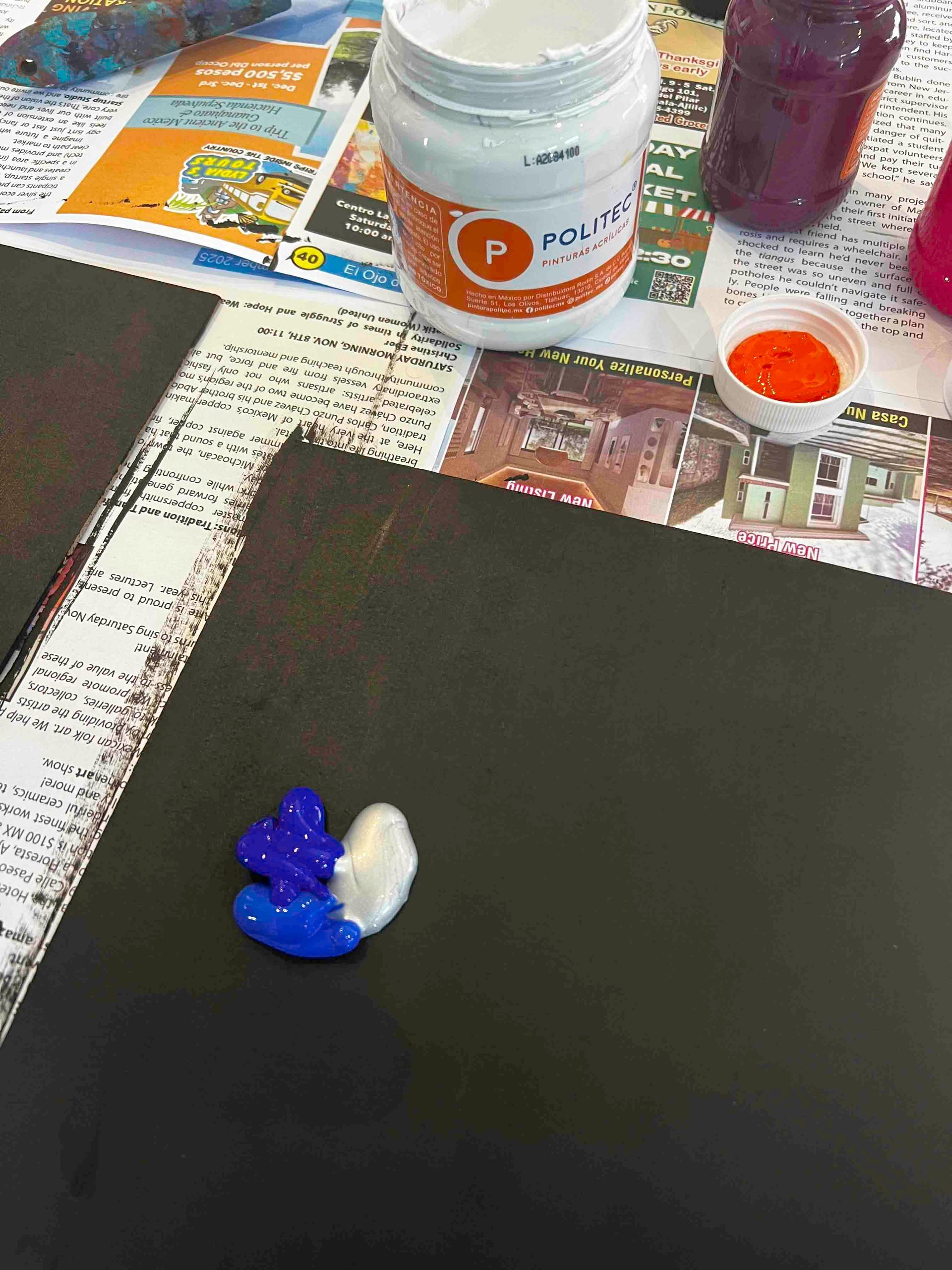 Blue, white, and dark paint on a black canvas with jars of paint and supplies scattered in the background.