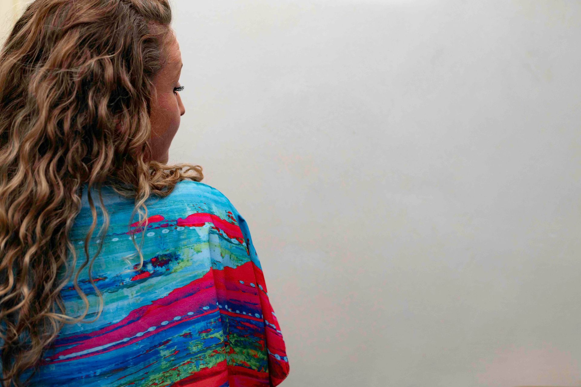Woman with curly hair and colorful shawl facing a blank whiteboard.