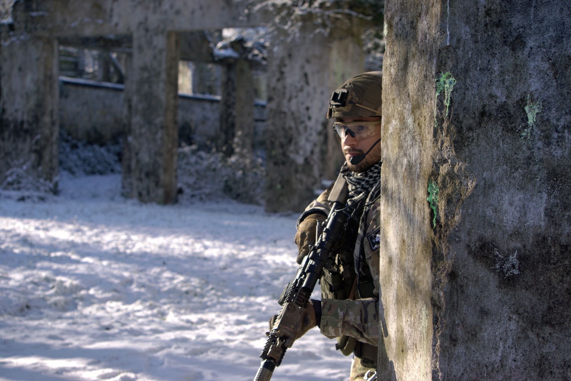 Ein Soldat lugt hinter einer Mauer im Schnee hervor.