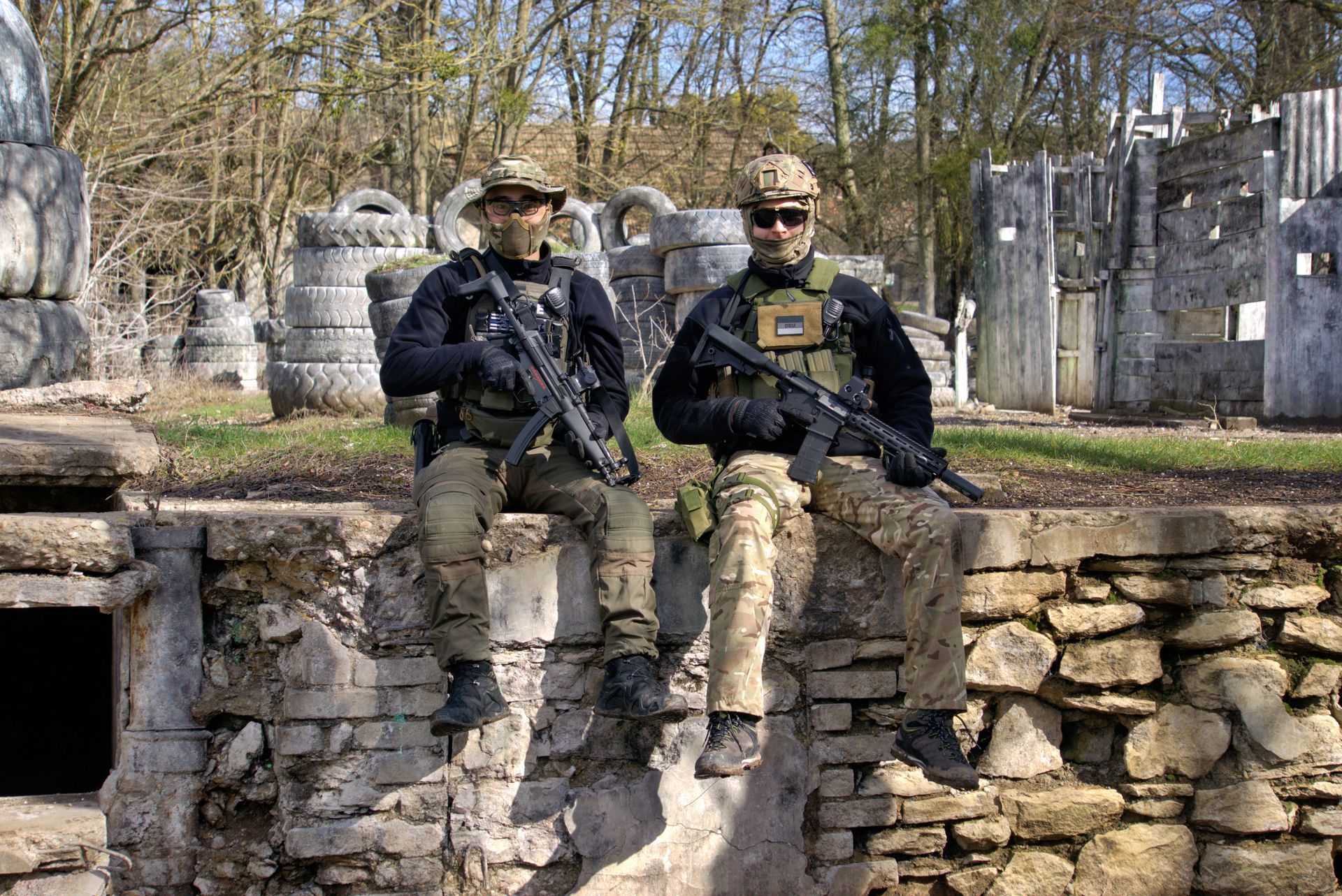 Zwei Soldaten sitzen auf einer Steinmauer auf einem Paintballfeld.