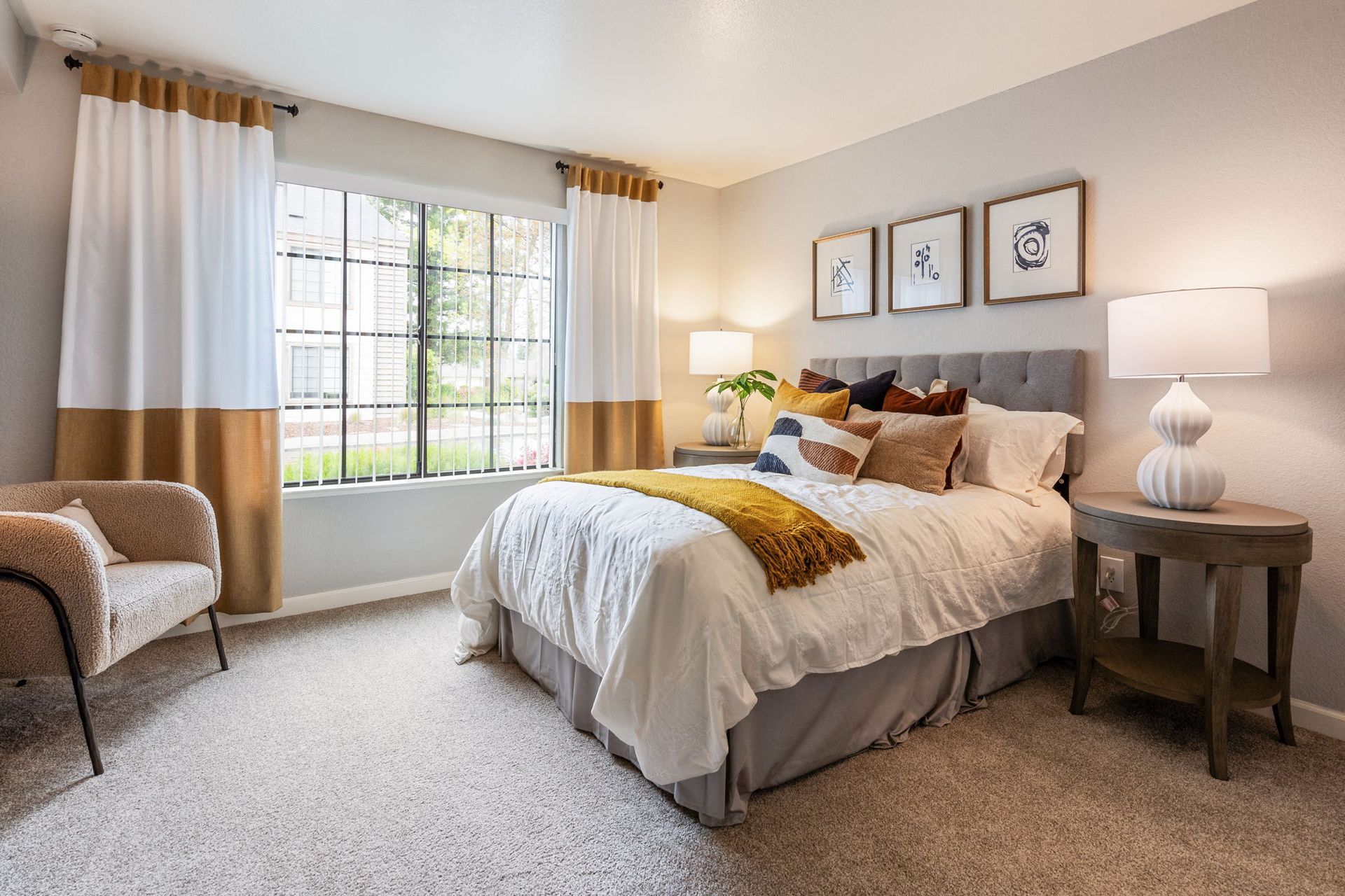Bedroom with a plush bed, two nightstands, lamps, and a large window with two-tone curtains.