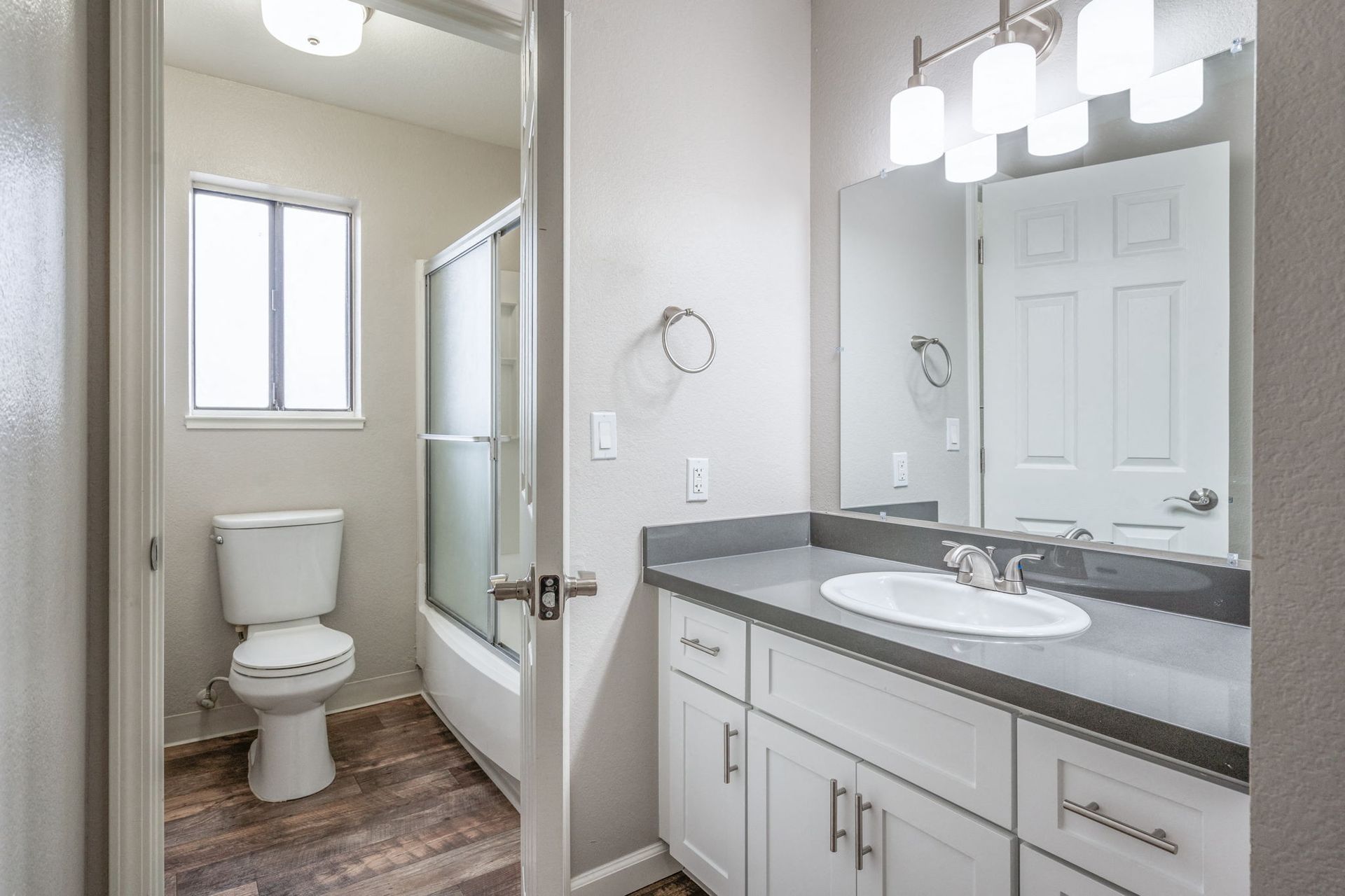 Bathroom interior with a white vanity, gray countertop, mirror, toilet, and glass-enclosed shower.