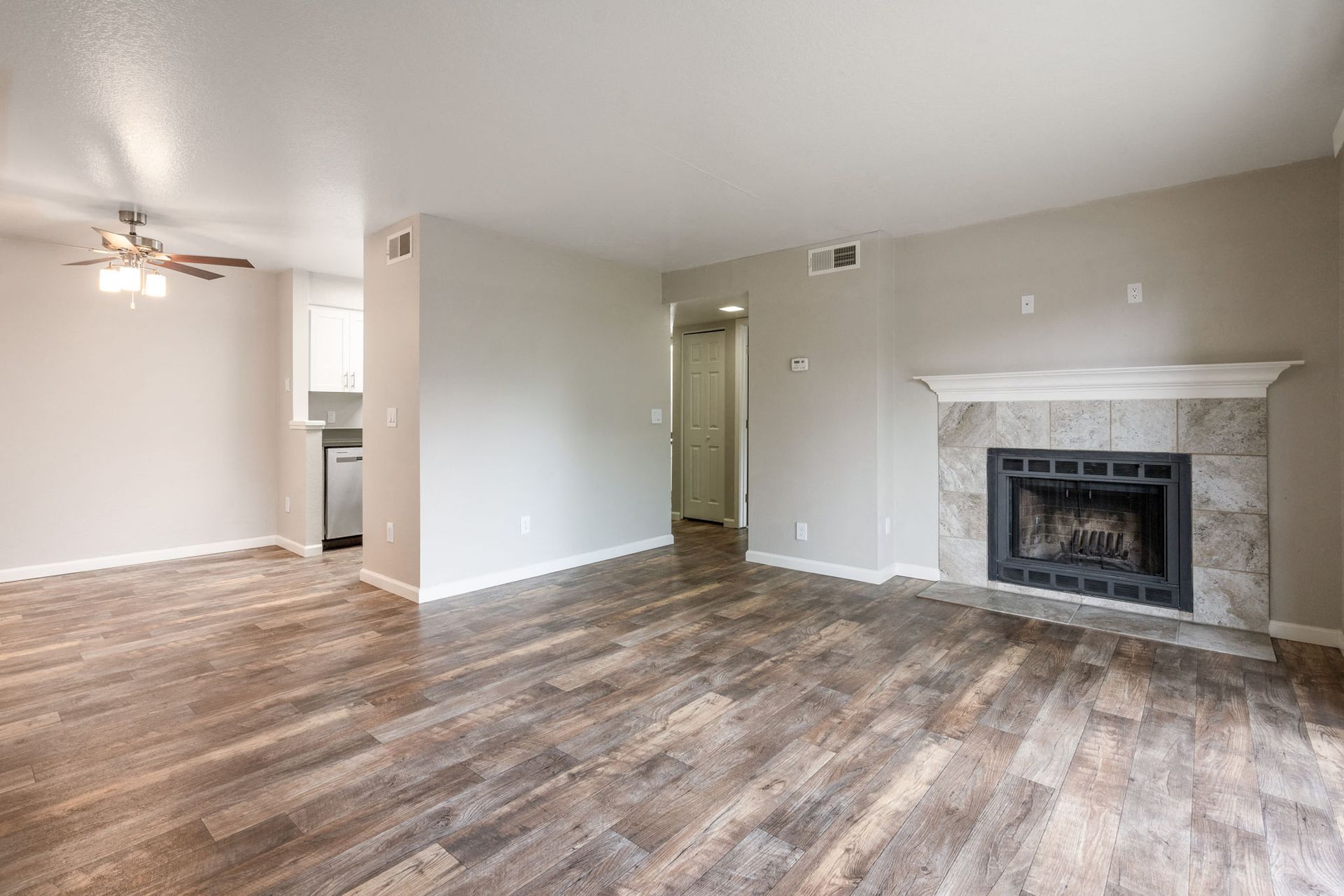 Living room with wood-look flooring, neutral walls, a ceiling fan, and a fireplace on the right.