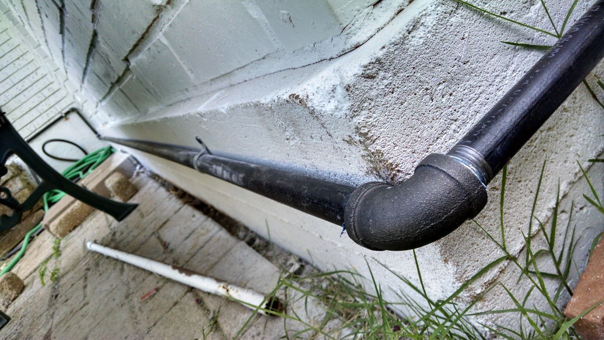 A black pipe is sitting on the ground next to a concrete wall.