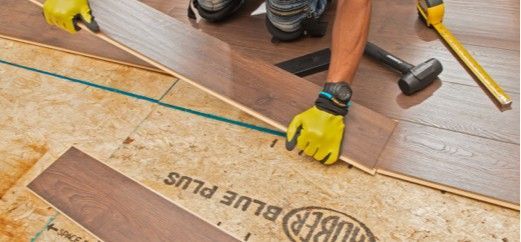 A person wearing yellow gloves is working on a wooden floor.