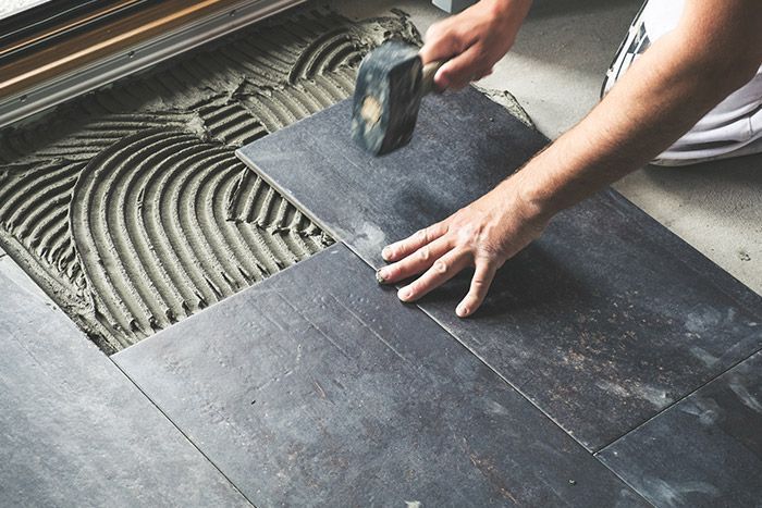 A person is laying tiles on the floor with a hammer.