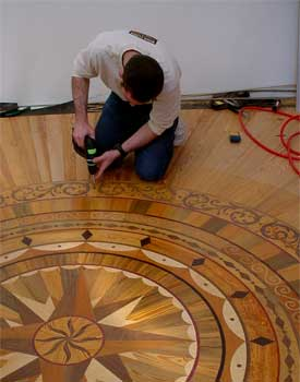 A man is working on a wooden floor with a drill