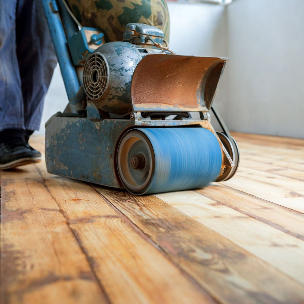 A person is sanding a wooden floor with a machine.