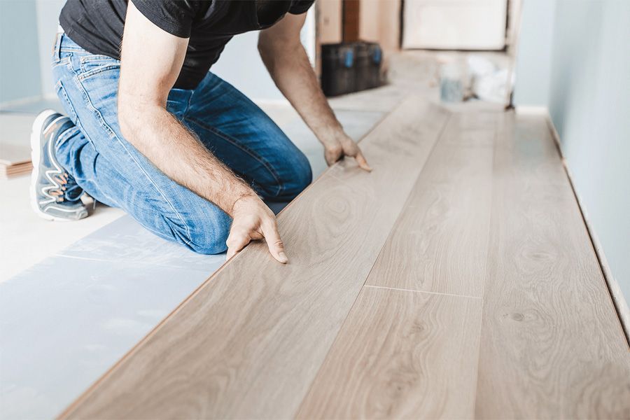 A man is kneeling down to install a wooden floor.