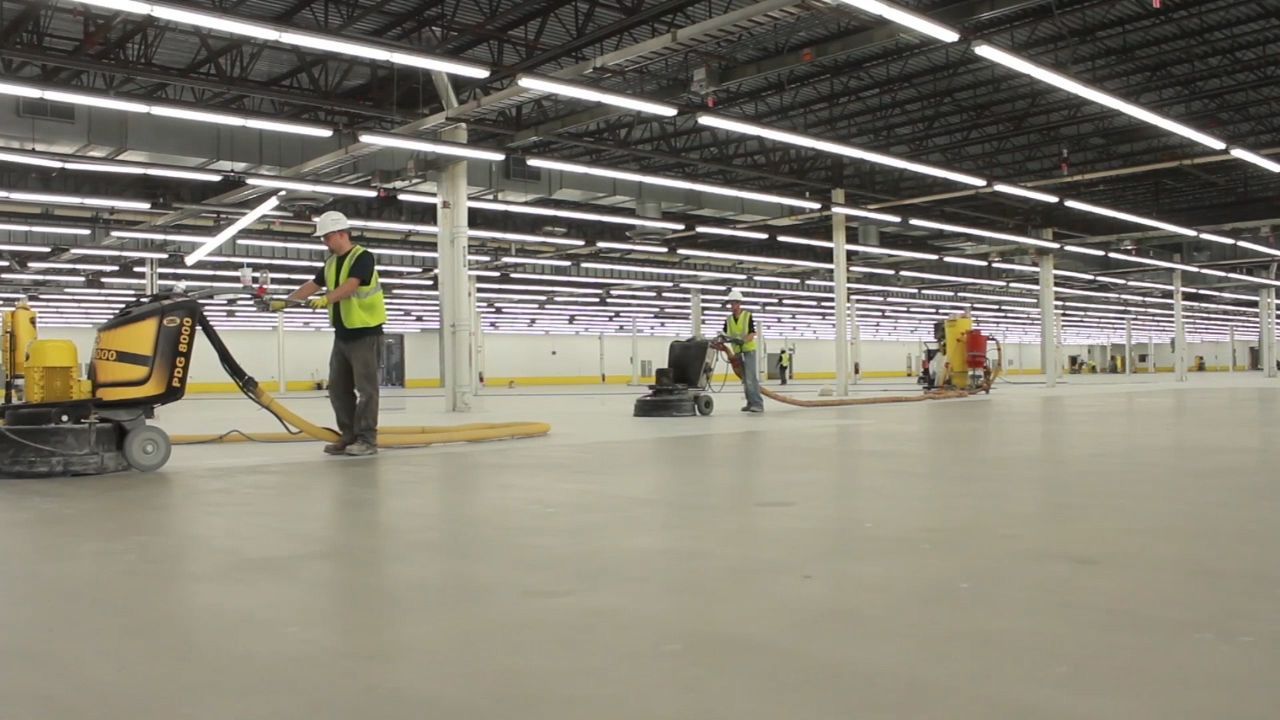 A group of construction workers are working on the floor of a large warehouse.