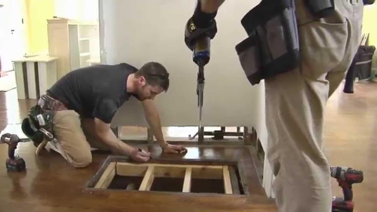 Two men are working on a wooden floor with a drill.