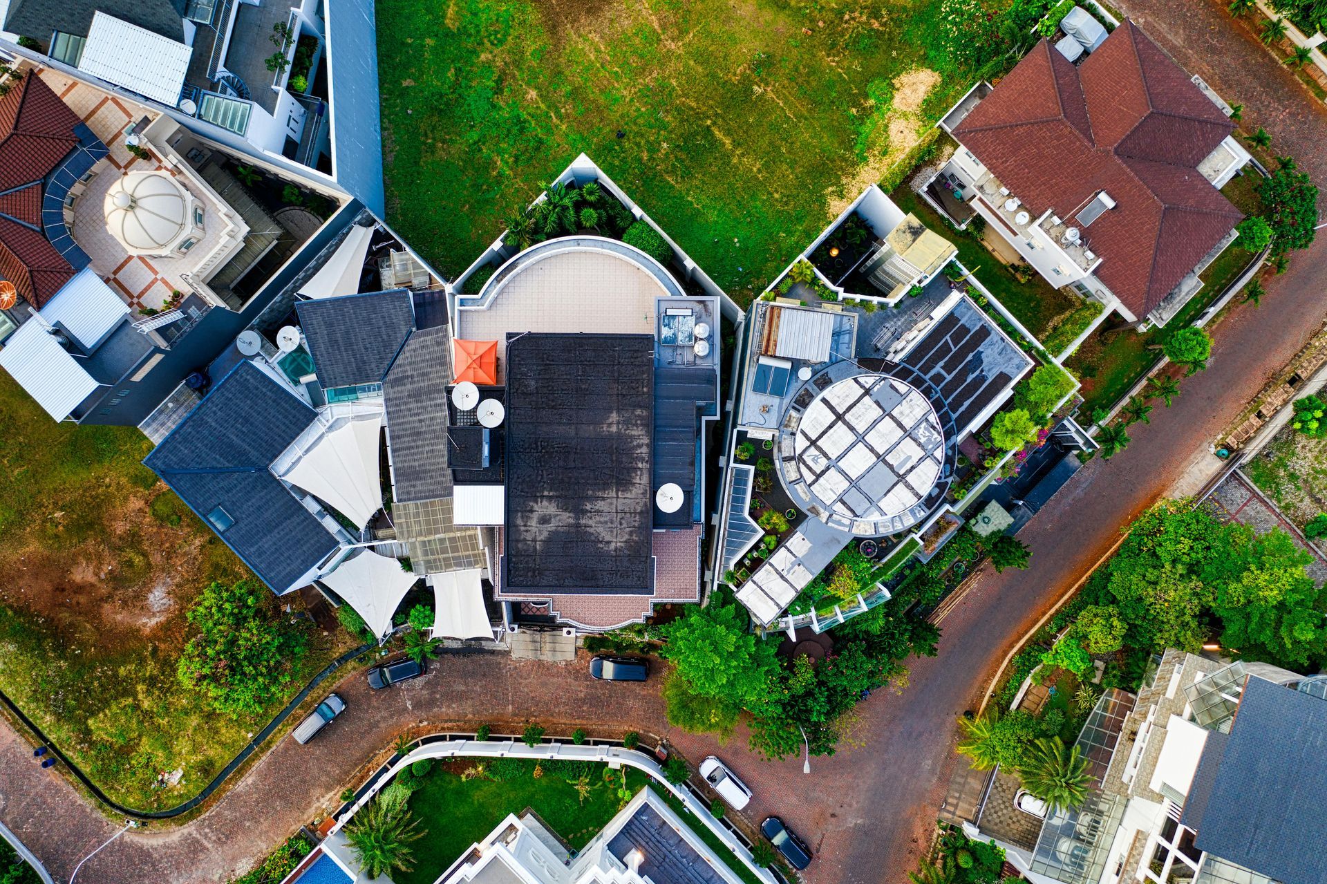 Aerial view of residential properties and winding roads, showcasing various house rooftops, green lawns, and vegetation.