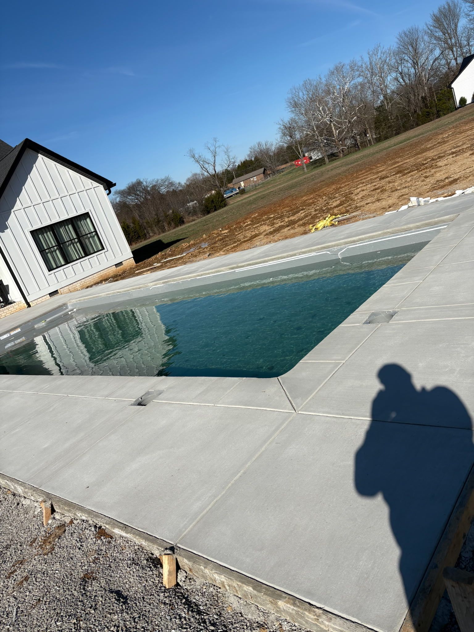 Swimming pool with blue water and gray concrete surrounding it on a sunny day. A building is in the background.