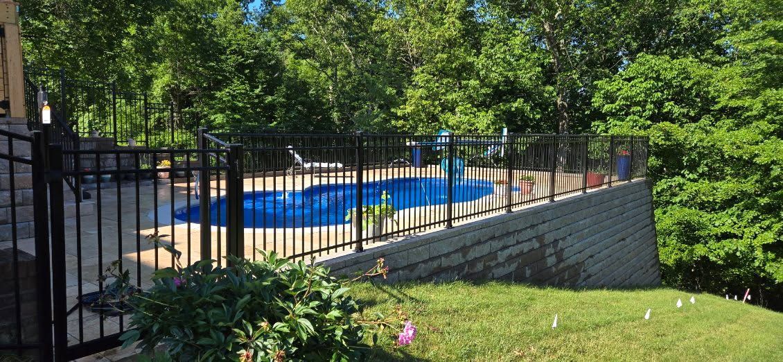Outdoor pool behind a black fence, with blue lounge chairs and trees in the background.