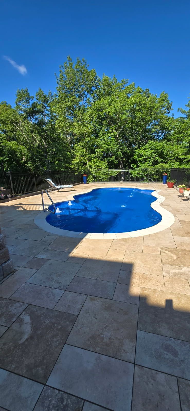 A blue-covered swimming pool surrounded by a stone patio and trees under a clear, blue sky.