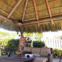 Outdoor tiki bar with thatched roof, palm trees, and people preparing drinks.