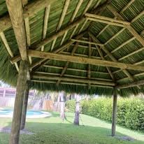 Wooden gazebo with thatched roof on a green lawn.