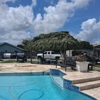 Poolside scene with a thatched roof shade structure, truck, and blue sky.