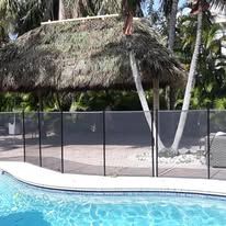 A pool with a black safety fence, beneath a thatched roof structure.
