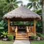 Tropical gazebo with thatched roof, wooden frame, and lush greenery in a backyard.
