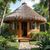 Wooden hut with thatched roof surrounded by greenery and a stone pathway.