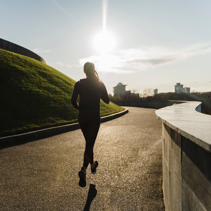 A woman is running down a road with the sun shining behind her