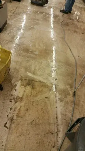 Wet, stained commercial floor; someone's legs and cleaning equipment are visible.