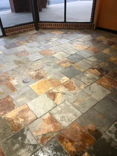 Slate tile floor, multi-colored, in a commercial setting; near glass windows. Some tiles are missing.