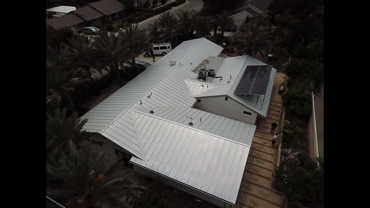 An aerial view of a house with a white roof and solar panels on it.