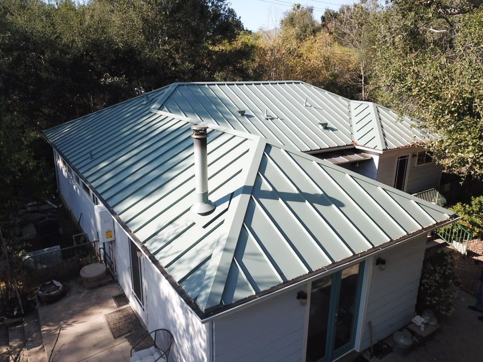 Green metal roof on a light blue house surrounded by trees.