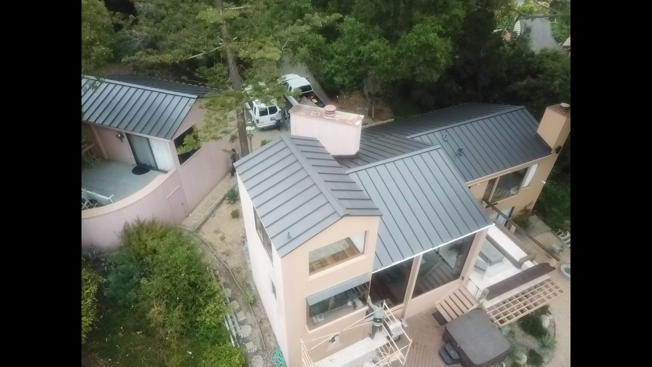 An aerial view of a house with a metal roof surrounded by trees.