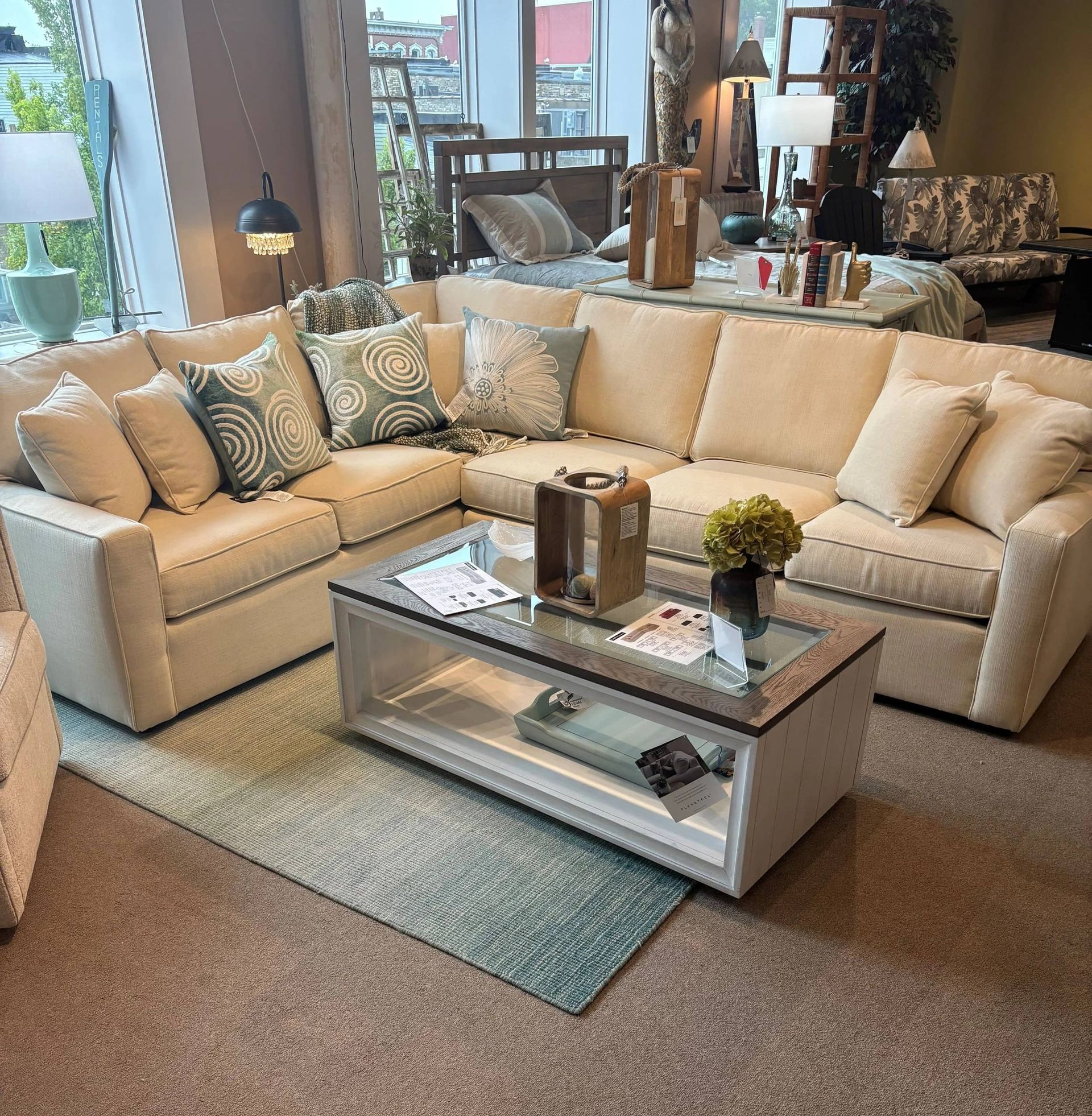 Cream-colored sectional sofa with decorative pillows, coffee table, and area rug in a furniture store setting.