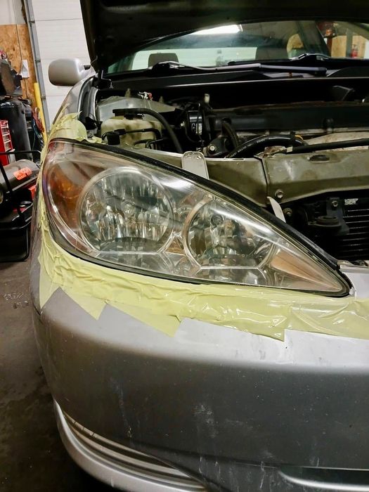Silver car with open hood, headlight taped for repair.