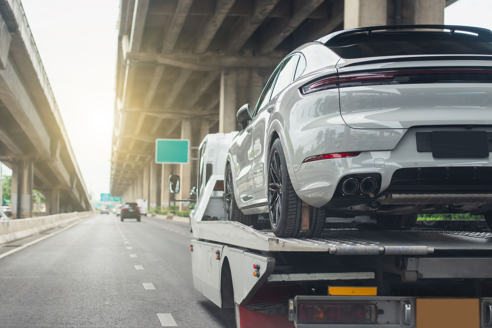 White car on a tow truck on a highway under an overpass.