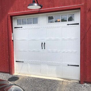 A white garage door is sitting in front of a red barn.