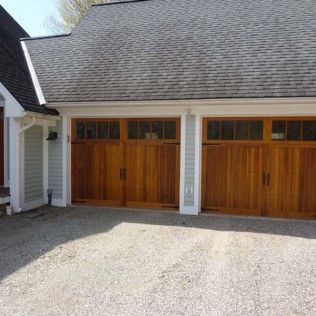 A house with three wooden garage doors and a gravel driveway.