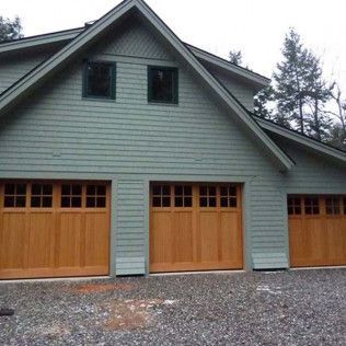 A green house with three wooden garage doors.