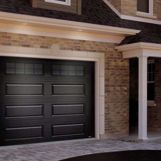 A black garage door is on the side of a brick house.