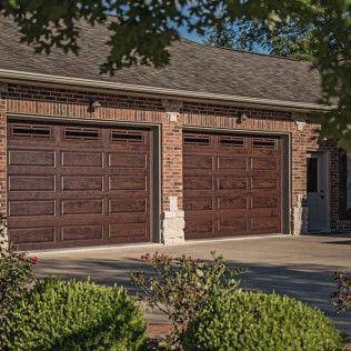 There are two garage doors on the side of a brick house.