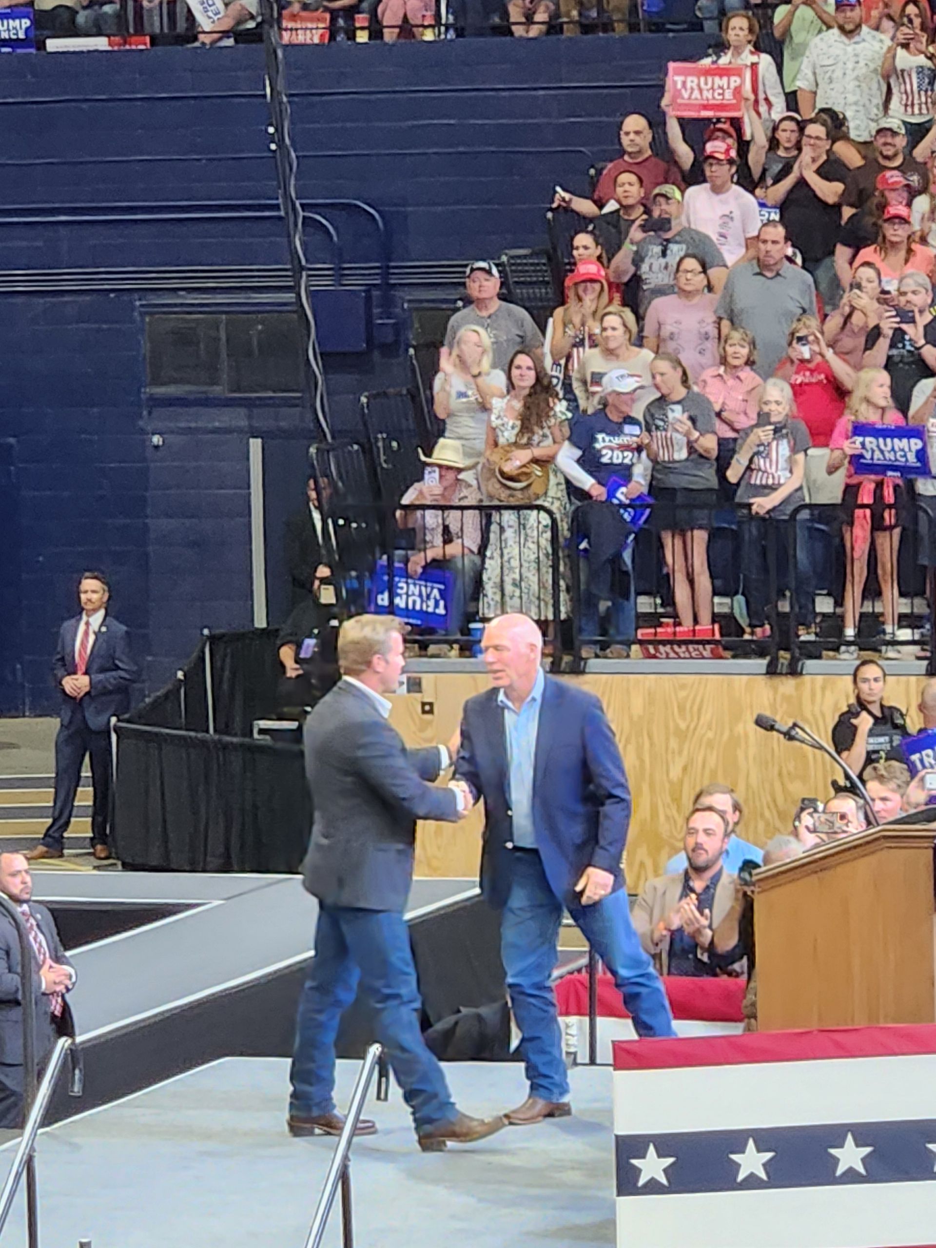 Two men shaking hands on a stage in front of a crowd