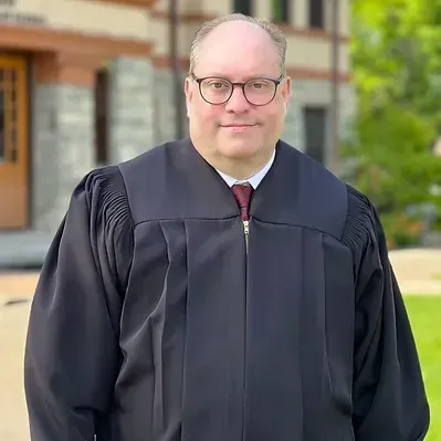A man in a graduation gown and tie is standing in front of a building.