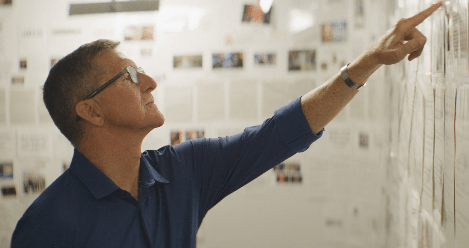 A man is pointing at a list on a whiteboard.