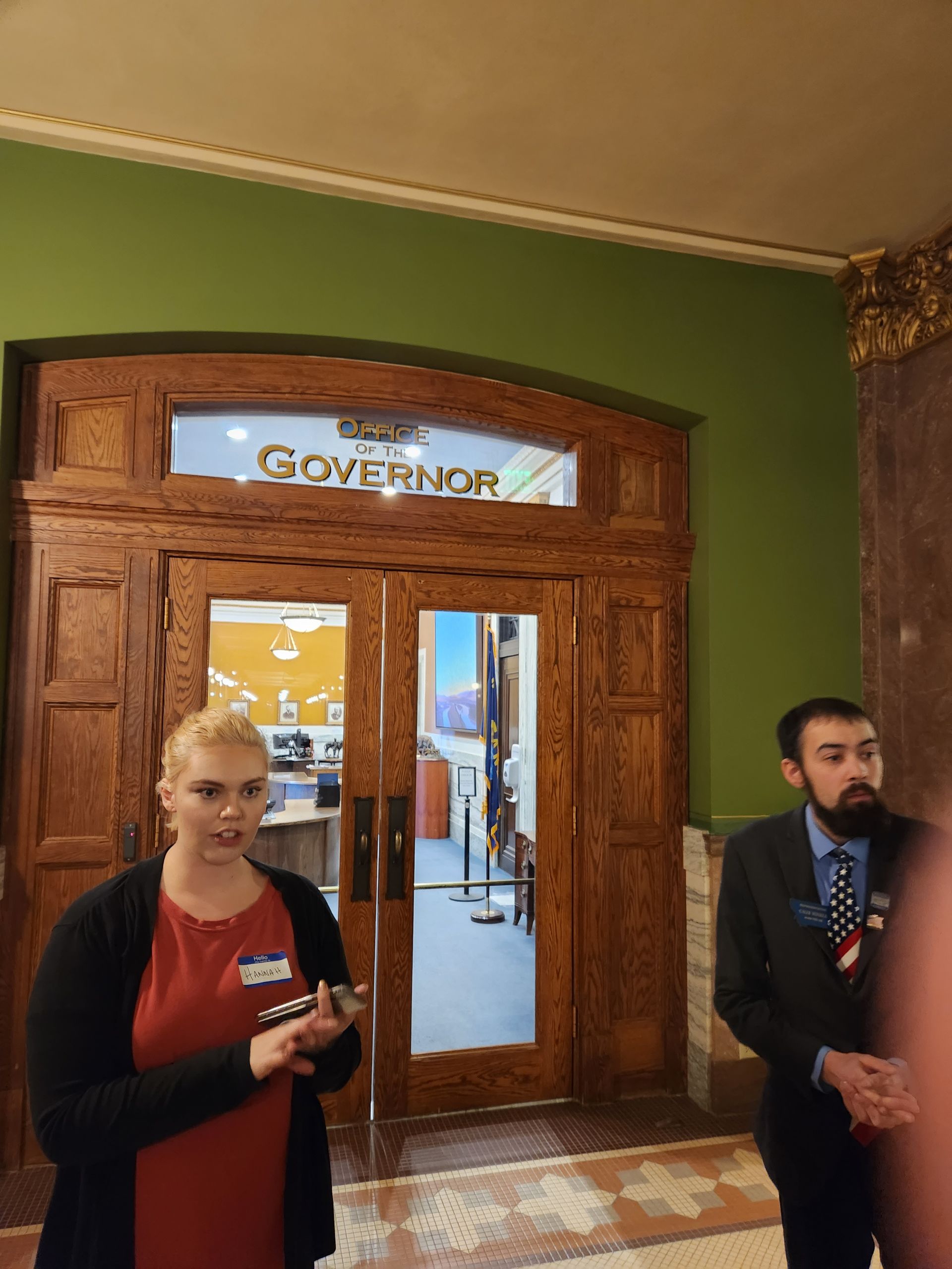 A man and a woman are standing in front of a door that says governor.