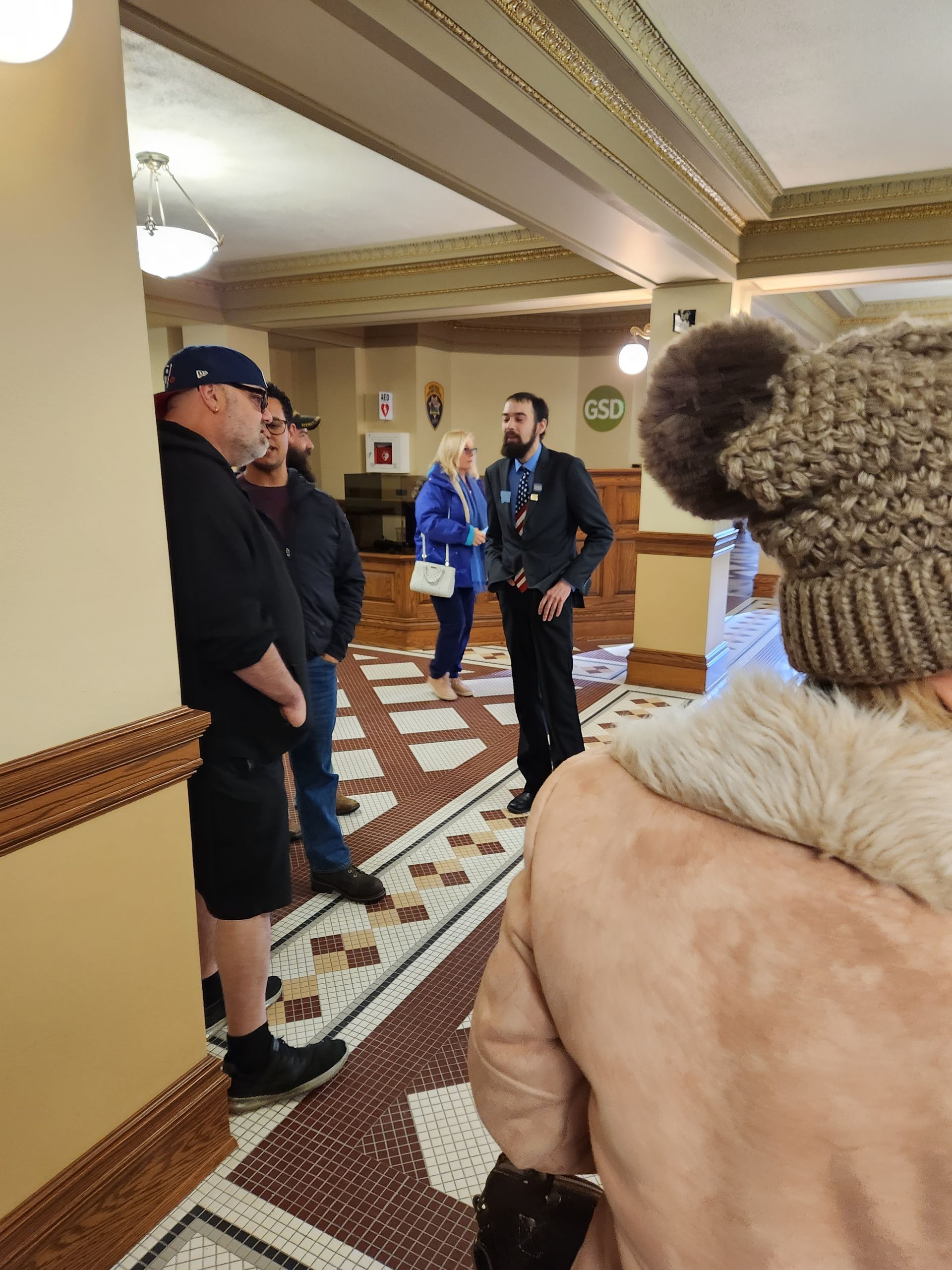 A group of people are standing in a hallway talking to each other.