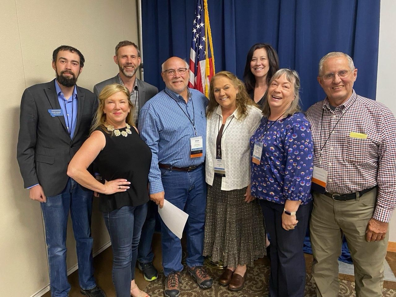 A group of people are posing for a picture in front of an american flag.