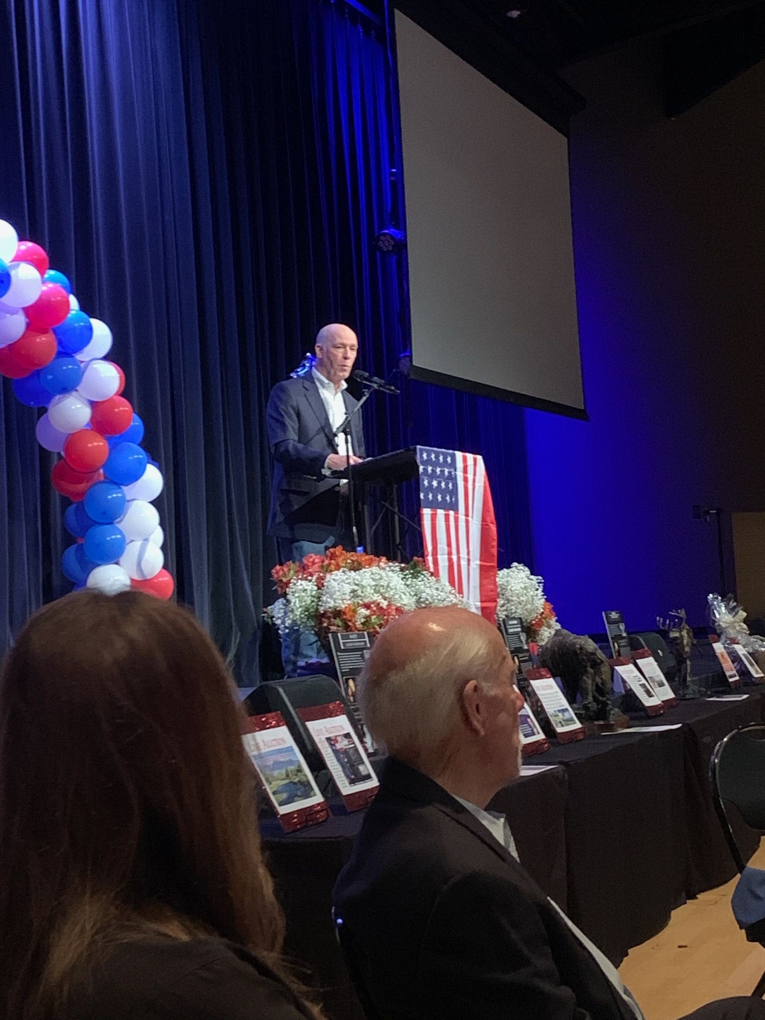 A man is giving a speech at a podium in front of an american flag.
