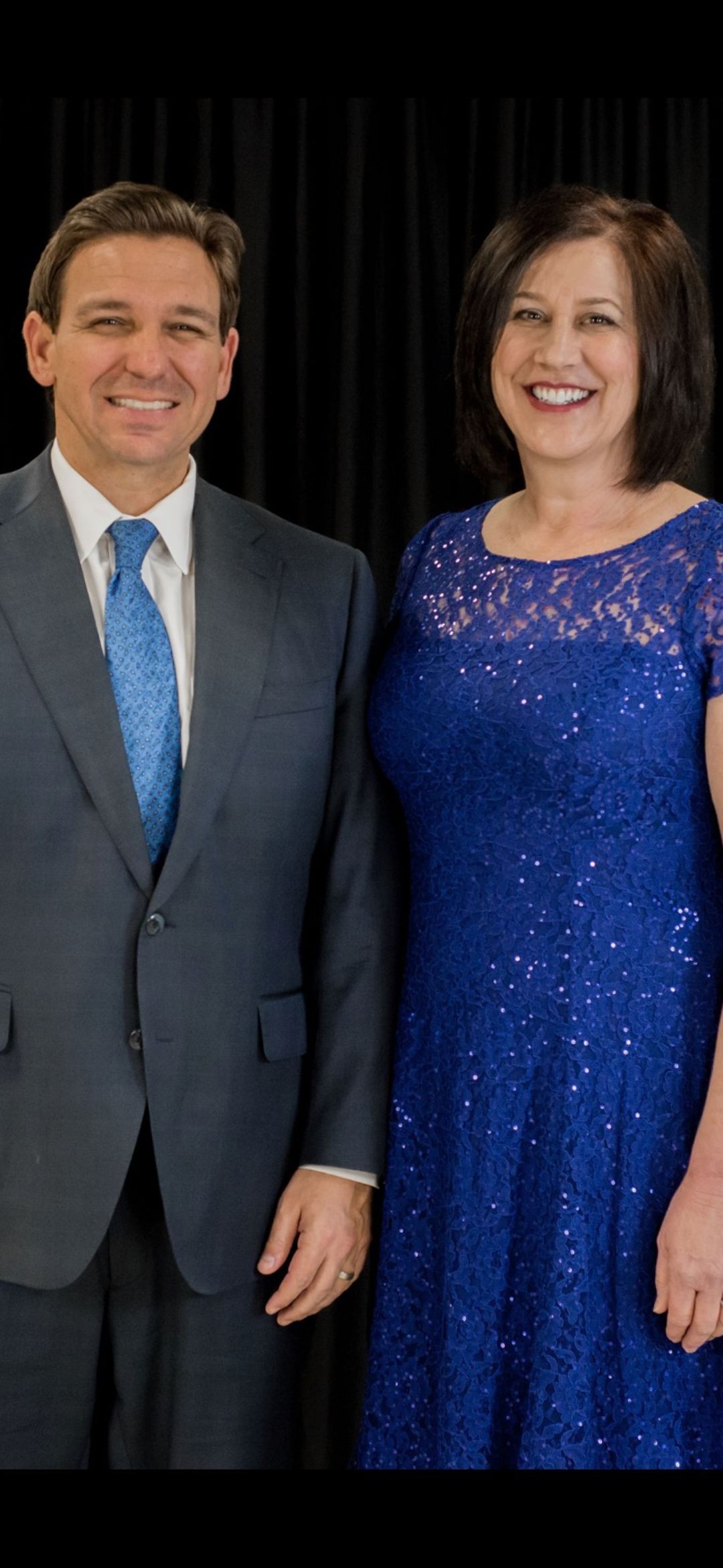 A man in a suit and tie is standing next to a woman in a blue dress.